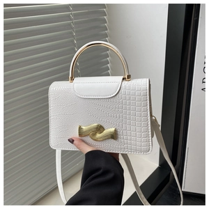 Detail of white crocodile-embossed bag featuring a gold metal handle and wave-shaped lock