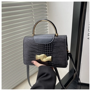 Detail of black crocodile pattern leather handbag with golden semicircular metal handle