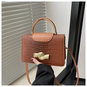 Detail of brown crocodile pattern handbag with golden semi-circular handle and clasp