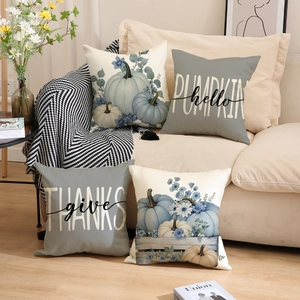Set di quattro cuscini decorativi autunnali con zucche e scritte su un divano beige