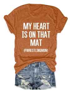 Flat lay of an orange wrestling mom t-shirt paired with distressed blue denim shorts