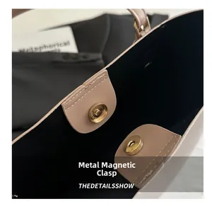 Detail of golden magnetic snap closure on a beige leather tote bag with black lining