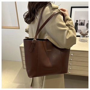 Detail of dark brown leather tote bag with gold lettering shown on shoulder in interior setting