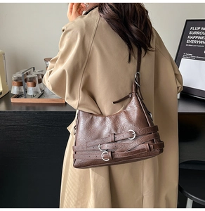 Dettaglio borsa a tracolla in pelle marrone scuro con fibbie d'argento e trench coat