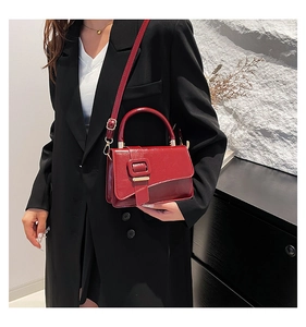 Close-up of a glossy red patent leather handbag with gold hardware on a black blazer