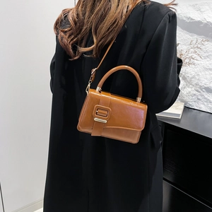 Minimalist dark brown leather shoulder bag with gold buckle worn by a model