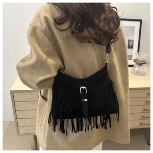 Detalle de bolso tote de ante negro con flecos y hebillas doradas en modelo femenino