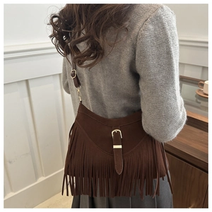 Detail shot of a dark brown suede tote featuring long fringe and a buckled leather strap