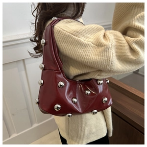 Detail of dark burgundy glossy underarm bag with silver metal ball ornaments on a model