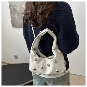 White hobo underarm bag with silver spherical rivets shown on a model's shoulder