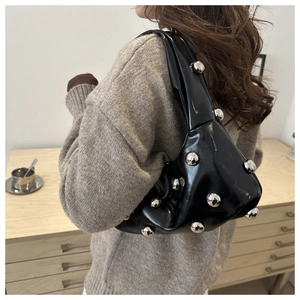 Detailed close-up of glossy black leather underarm bag with large silver ball rivet studs