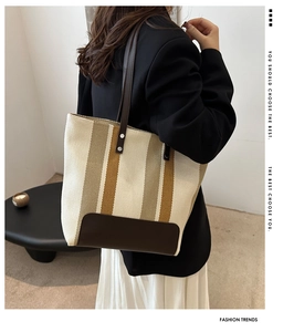 Close-up of a large striped canvas tote bag with brown leather straps and silver rivets