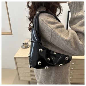 Fashionable black glossy underarm bag with silver metal bead rivets on a female model