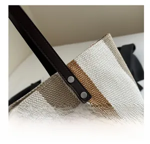 Close-up of striped canvas tote bag with leather handle and metal rivet reinforcement