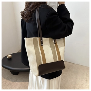 Close-up of striped canvas tote bag with brown leather straps shown on a model's shoulder
