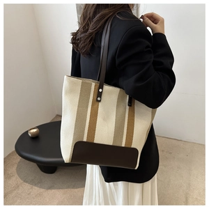 Close-up of vintage striped canvas tote with brown leather handles worn on shoulder