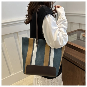 Detail of striped canvas tote bag with brown leather base and reinforced handles