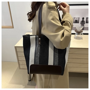 Chic striped canvas tote bag with brown leather handles worn by a model in beige trench coat