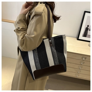 Detail of striped canvas tote bag with brown leather straps and metal rivets on side