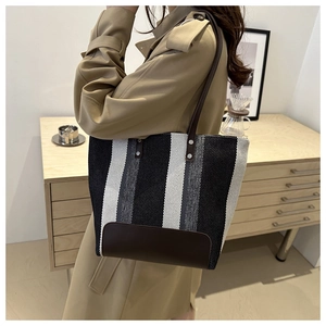 Detail of striped canvas tote bag with leather straps on a khaki trench coat model