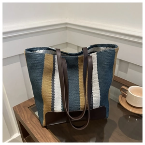 Detail of colorful striped canvas tote bag with brown leather base on wooden table