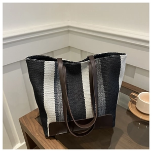 Detail of striped woven tote bag with brown leather straps on a wooden table