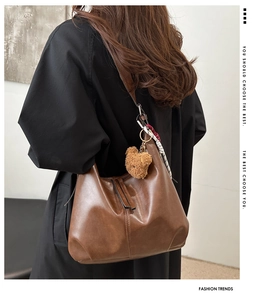 Detail of dark brown Hobo shoulder bag with plush bear charm and striped scarf accessory