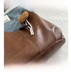 Close-up of dark brown leather tote bag showing pleated texture and woven drawstring detail