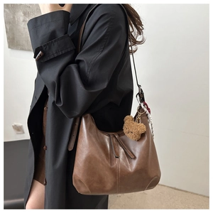 Brown leather crescent bag detail with plush bear charm and decorative silk scarf