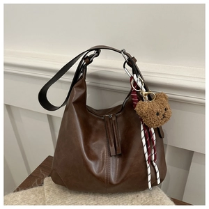 Detailed view of dark brown hobo bag featuring a plush bear charm and dual zipper decor