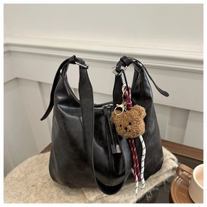 Close-up of black leather tote bag with a cute brown plush bear charm detail
