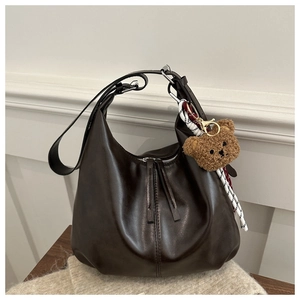 Close-up of a dark brown leather hobo bag with a plush bear charm and woven cord detail