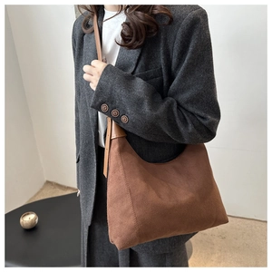 Detailed texture of brown matte leather shoulder bag worn with a gray blazer