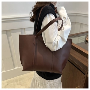Side view of large dark brown leather tote bag worn by a model in a minimalist urban setting