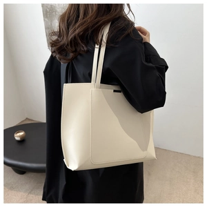 Detailed close-up of cream-white leather tote bag with minimalist stitching and front pocket