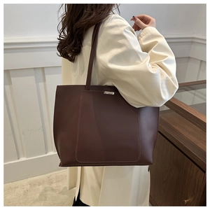 Detail of a large dark brown tote bag with metal buckle and shoulder strap worn by a model