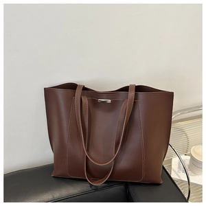 Detail of a large dark brown faux leather tote bag on a black sofa for office commuting