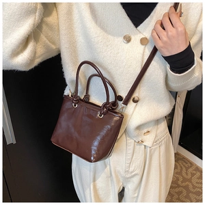 Détail d'un sac seau en cuir brillant marron foncé avec poignées et finitions dorées