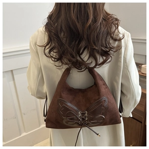 Detail of dark brown suede handbag featuring large leather bow and cross-tie metal eyelets