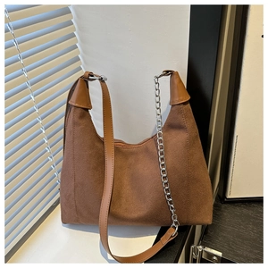 Detail of brown canvas hobo bag featuring a leather strap and silver metal chain