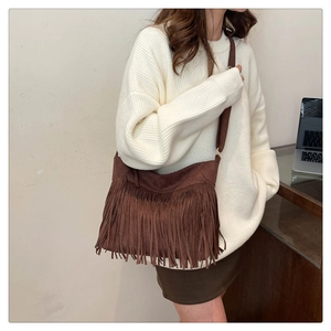 Detail view of coffee brown suede fringe crossbody bag worn by model in a chic room