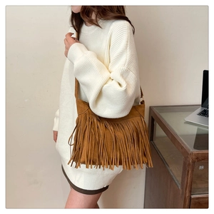 Close-up of brown suede shoulder bag with long fringes and adjustable strap on a model