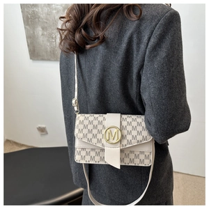 Gros plan sur un sac crème avec motif M gris et fermoir doré porté avec un manteau gris