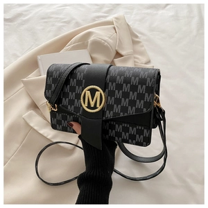 Gros plan du fermoir logo M doré et du motif monogramme gris sur un sac à bandoulière noir