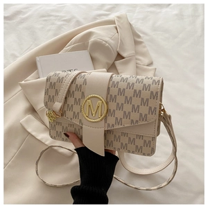 Détail du sac beige avec imprimé lettres M et fermoir métallique doré circulaire