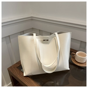 Detail of a white minimalist faux leather tote bag on a glass table with a coffee cup