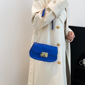 Sac carré en cuir bleu Klein avec chaîne dorée porté sur un trench-coat de couleur beige