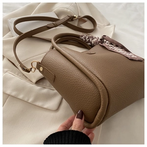 Sac seau en cuir marron avec foulard à carreaux posé sur un blazer beige
