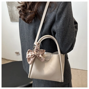 Détail du sac seau en cuir beige avec foulard à carreaux et logo gaufré chic