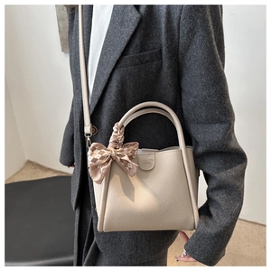 Détail d'un sac seau en cuir beige avec un foulard en soie à carreaux sur la poignée